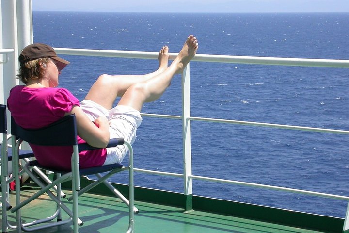 Mensch im Stuhl entspannt an Deck eines Schiffes und blickt aufs Meer