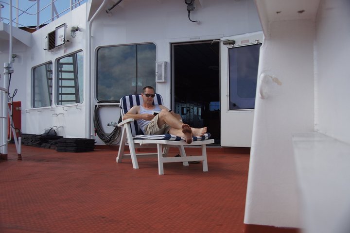 Passagier auf Frachtschiff am Lesen im Liegestuhl